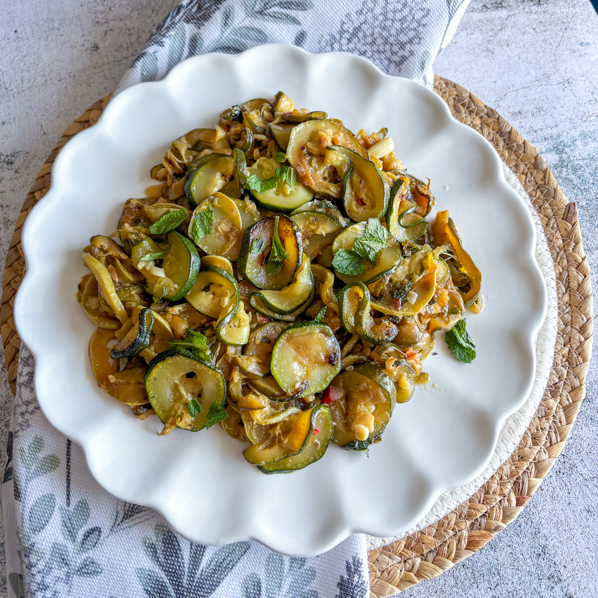 Top-down view of slow-braised courgettes with mint plated on a scalloped dish