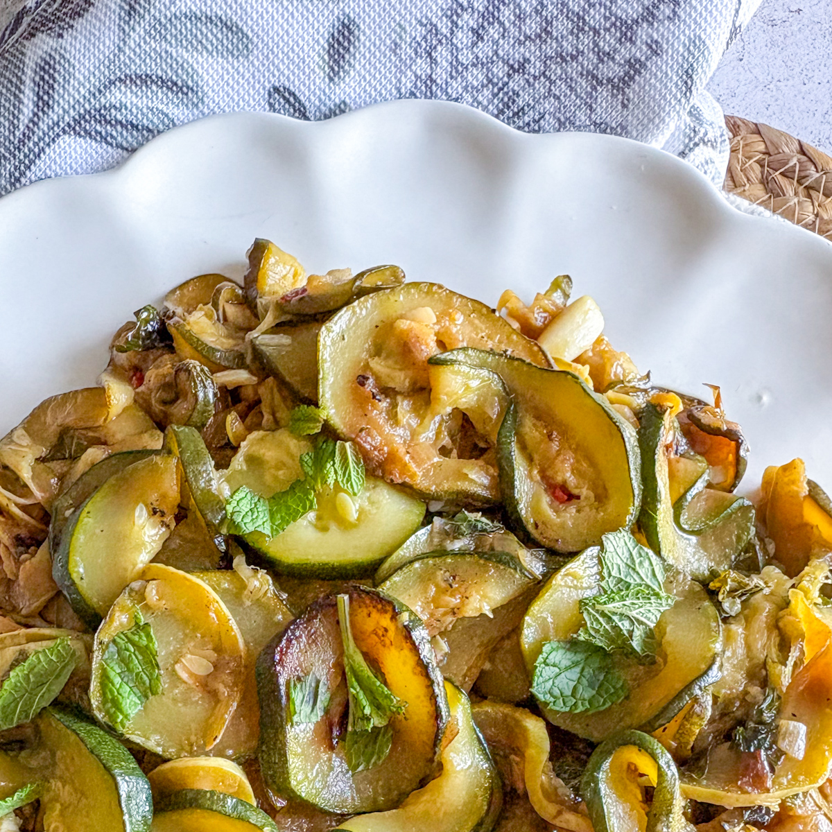 Slow-braised courgettes with mint and chilli plated on a white scalloped dish