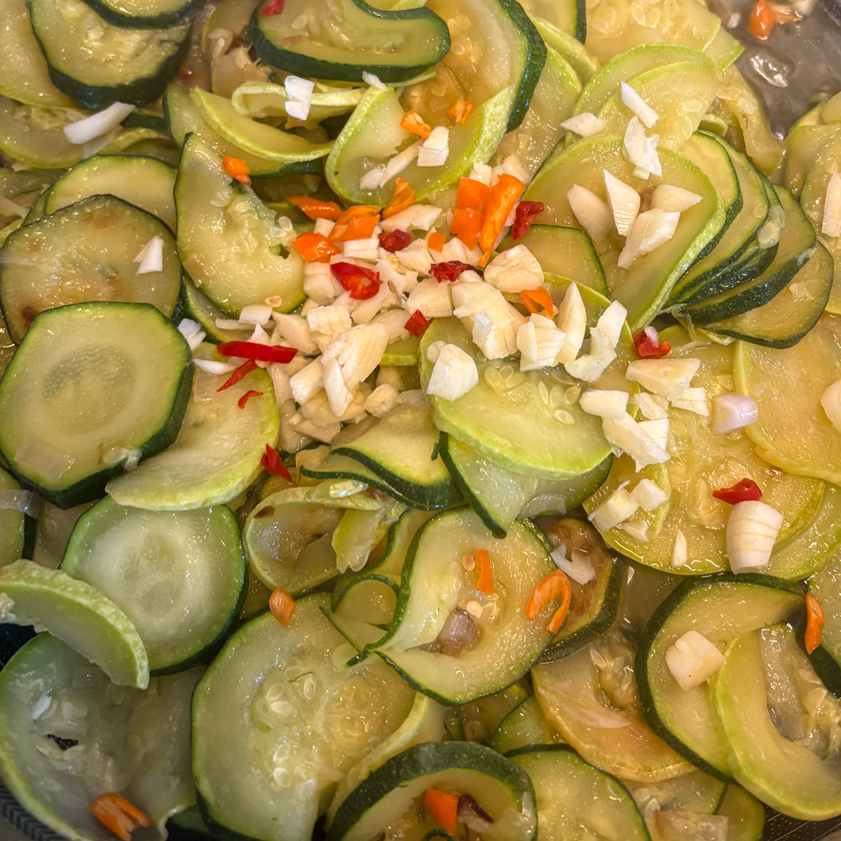 Sliced courgettes with shallot, garlic and red chilli ready for slow-braising in a pan