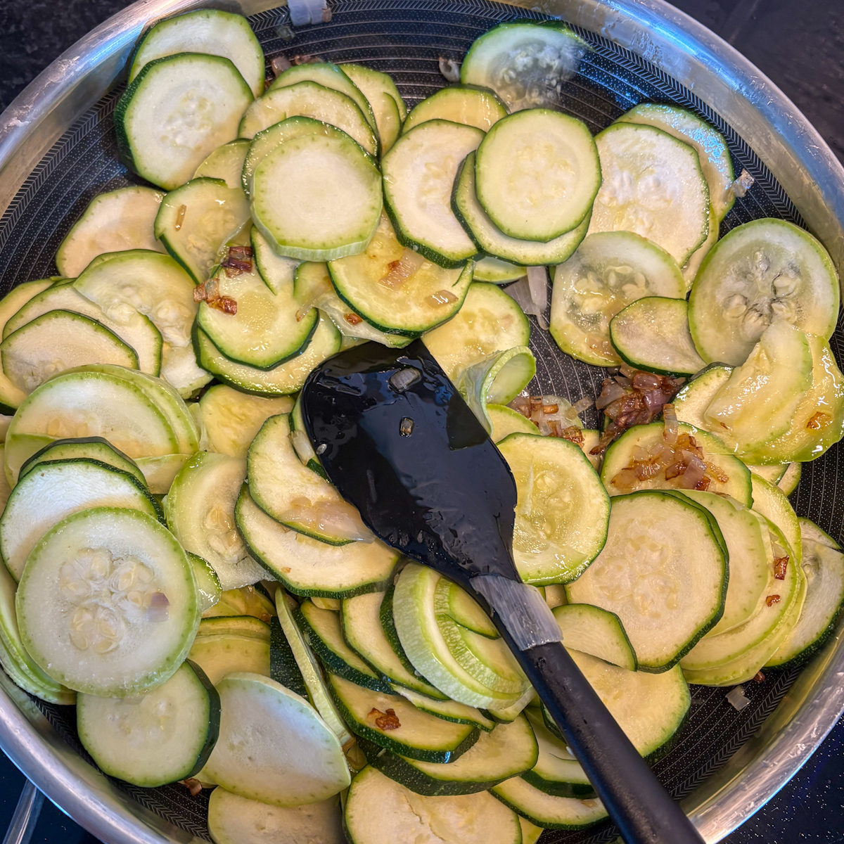 Thinly sliced courgettes added to a pan with sautéed shallot for slow-braising