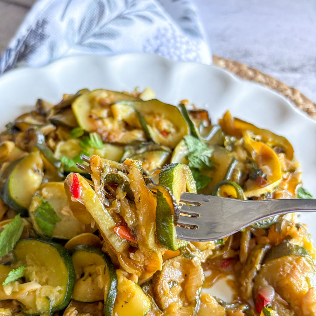 Forkful of slow-braised courgettes with mint, garlic and chilli lifted from a white plate