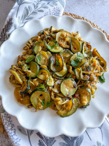 Slow-braised courgettes with mint served on a white scalloped plate as a cold Mediterranean appetiser