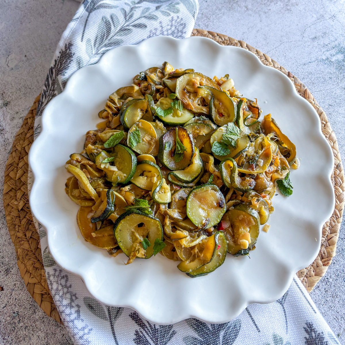 Slow-braised courgettes with mint served on a white scalloped plate as a cold Mediterranean appetiser
