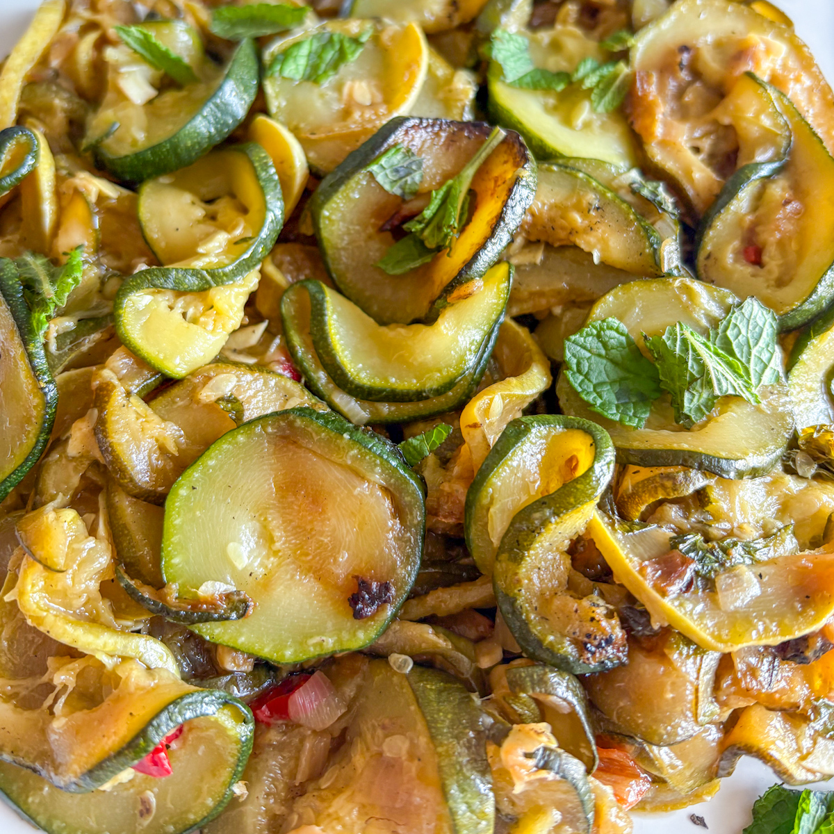  Close-up of slow-braised courgettes with fresh mint leaves on a white serving plate