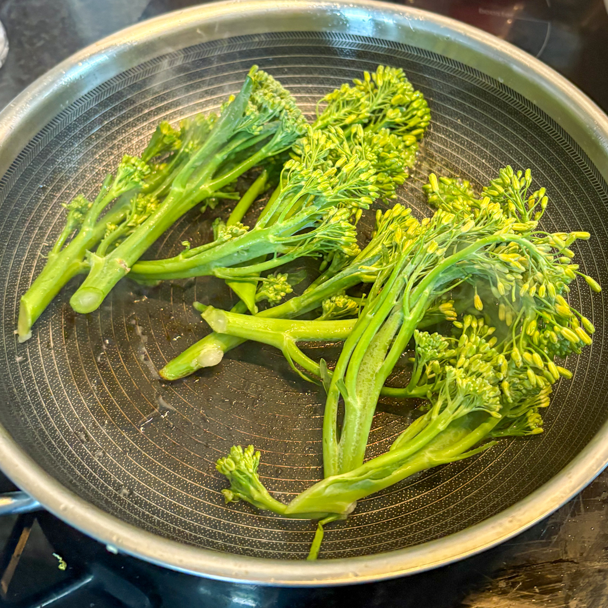Trimmed broccolini stems in a hot frying pan starting to char on medium-high heat