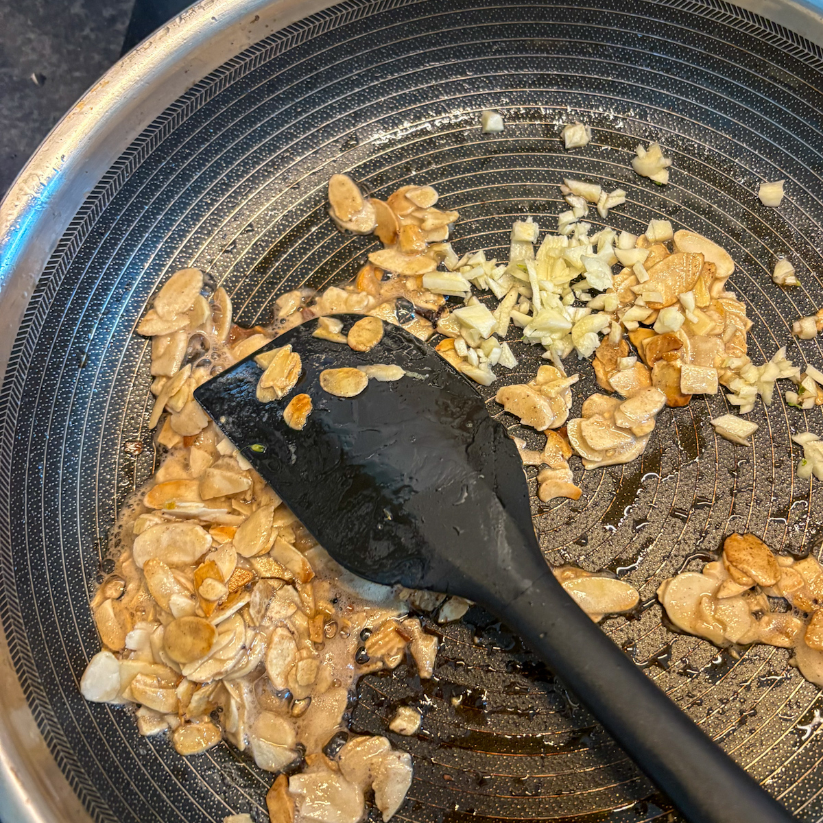 Toasted sliced almonds and minced garlic cooking in butter for charred broccolini
