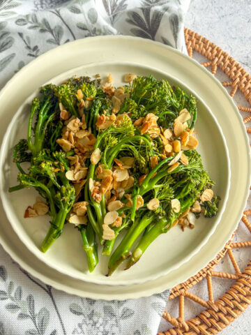 Charred broccolini with garlicky almonds served on a cream plate with linen napkin