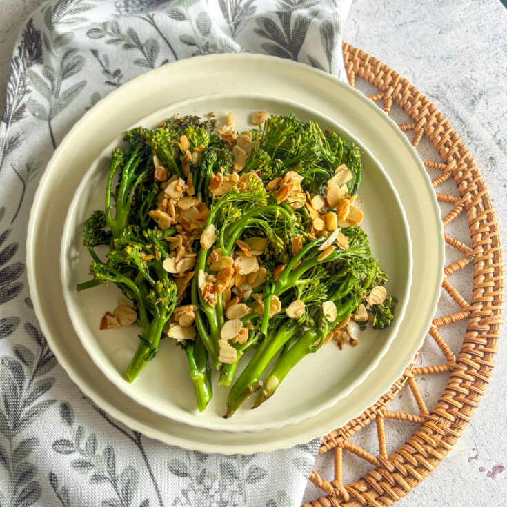 Charred broccolini with garlicky almonds served on a cream plate with linen napkin