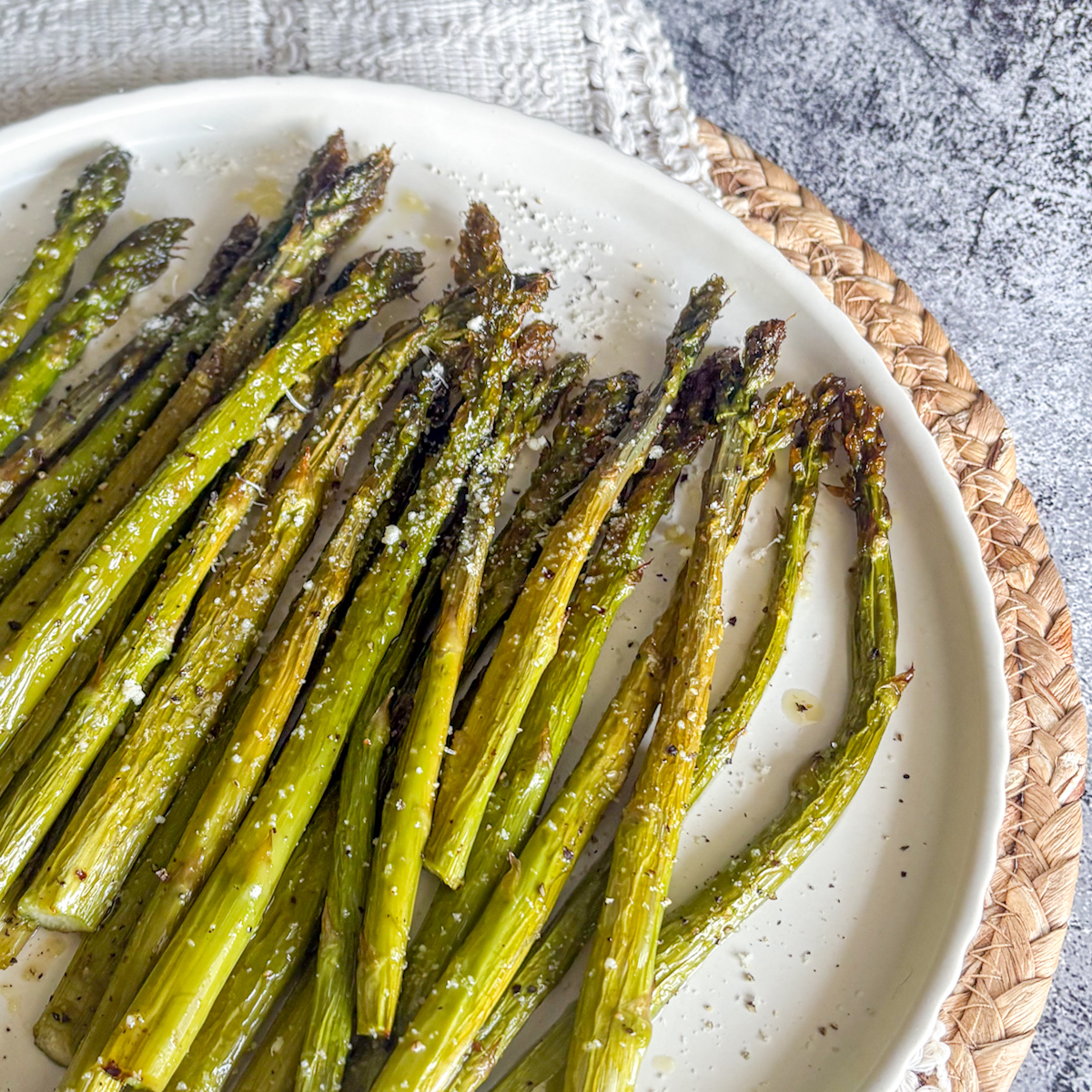Oven roasted asparagus on a white plate with parmesan cheese and sea salt, ready to serve.