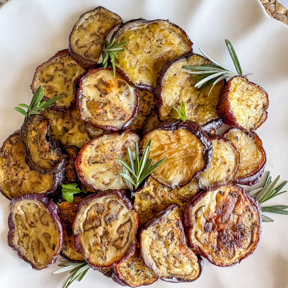 Close-up of roasted aubergine recipe with golden edges and rosemary garnish