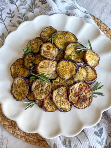 Easy roasted aubergine rounds on white plate with fresh rosemary and thyme sprigs