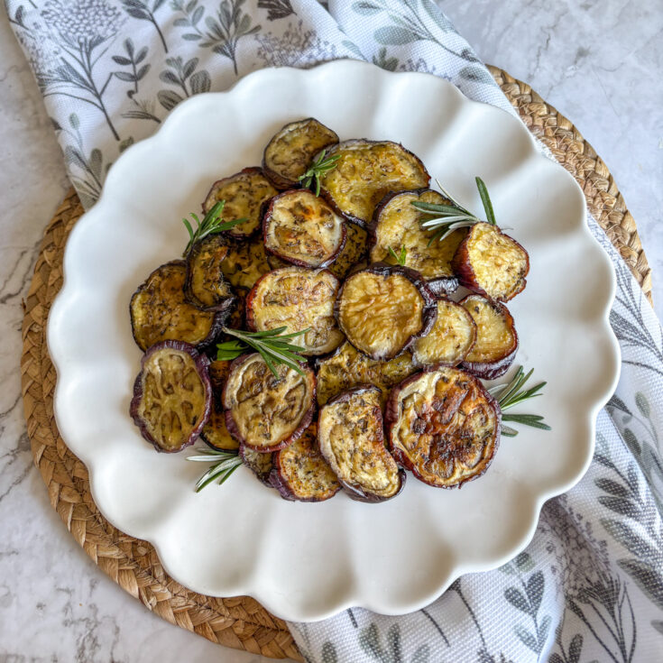 Easy roasted aubergine rounds on white plate with fresh rosemary and thyme sprigs