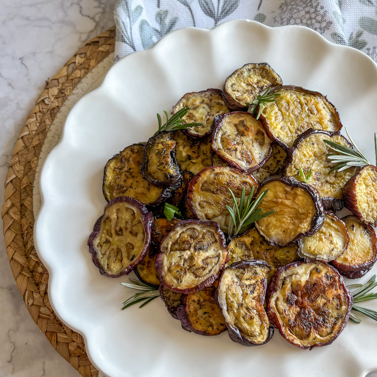 Easy roasted aubergine on white scalloped plate over woven straw mat