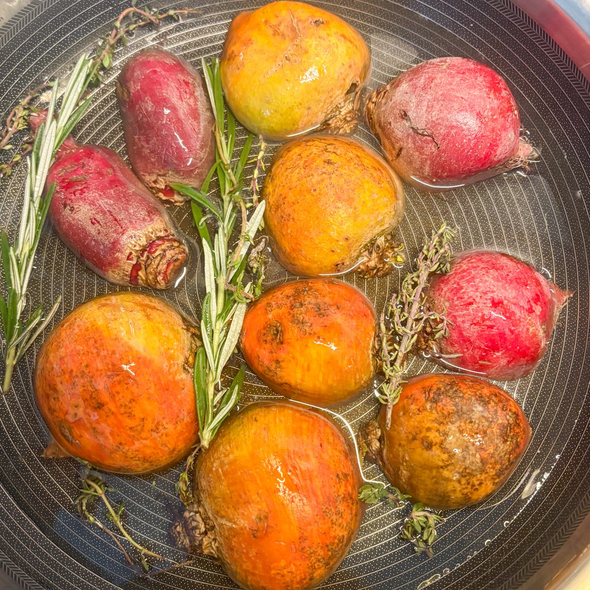  mixed-colour beetroot in skillet with rosemary and thyme sprigs in water, ready to braise.