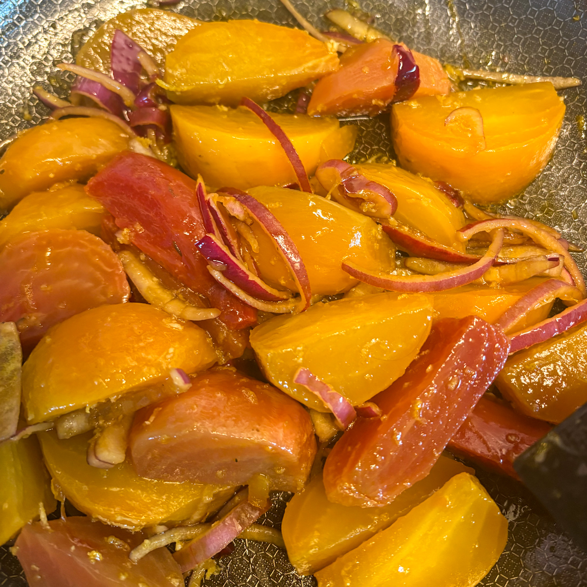 Braised beetroot wedges in skillet coated in glossy white wine vinegar glaze with red onion.