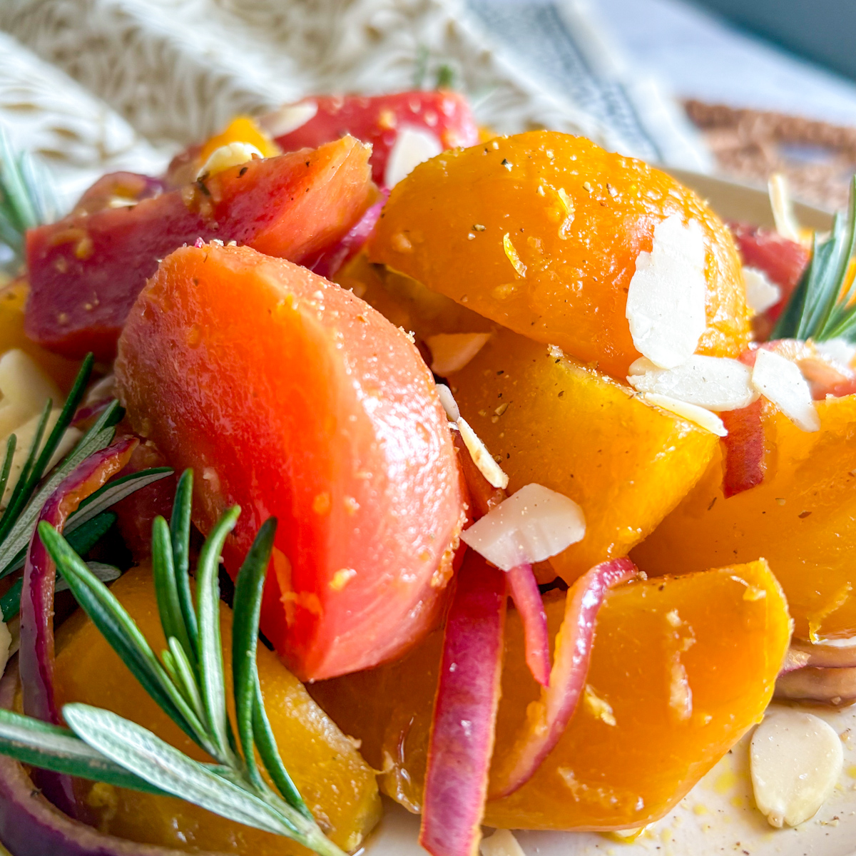 Close-up of braised beetroot with glossy glaze, rosemary, red onion ribbons and flaked almonds.