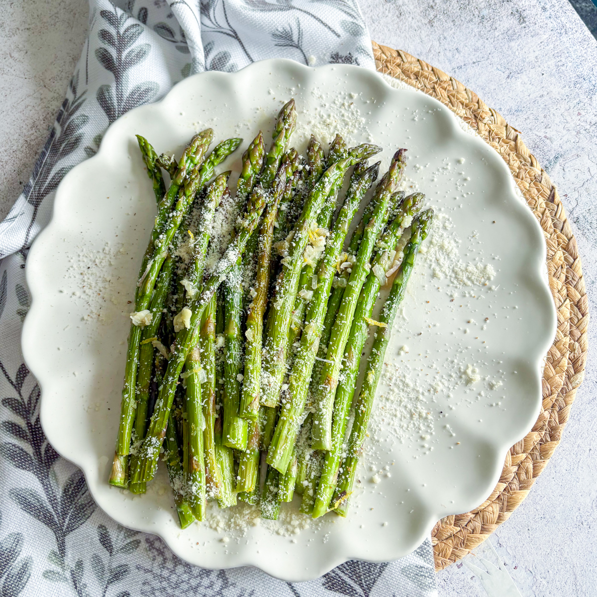 Pan-steamed asparagus side dish with garlic butter, lemon and Parmesan on a scalloped white plate.