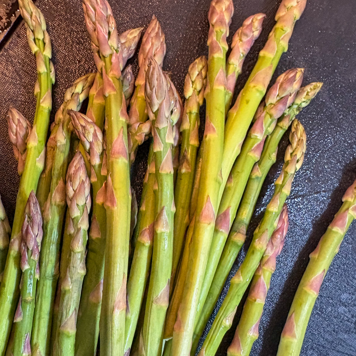 Fresh green asparagus spears on a dark surface, ready for the pan-steamed asparagus recipe.