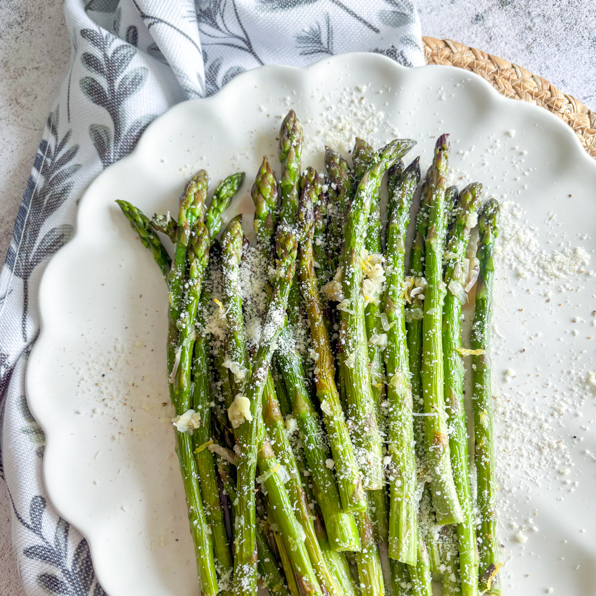 Easy pan-steamed asparagus side dish topped with shaved Parmesan, lemon zest and garlic butter on a white plate