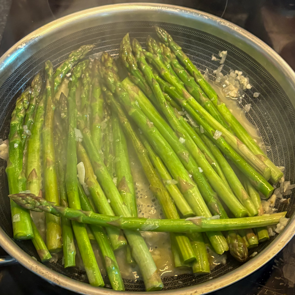Pan-steamed asparagus cooking in a stainless steel skillet with garlic, shallot and butter sauce.