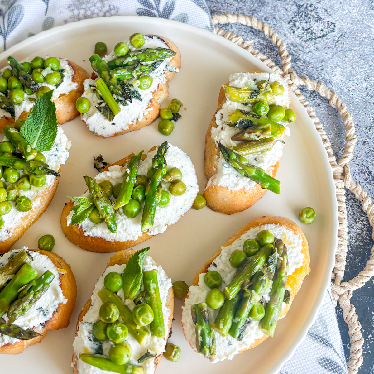 Plate of pea and asparagus crostini topped with creamy ricotta, asparagus tips and sweet peas