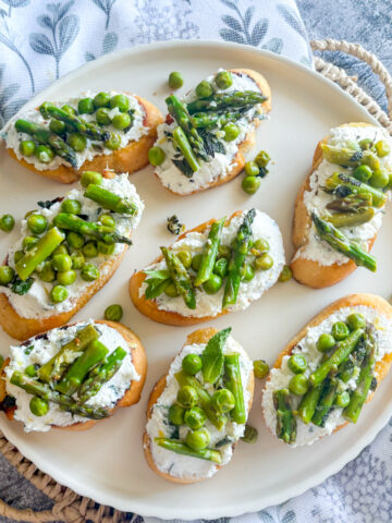 Plated pea and asparagus crostini with whipped lemon ricotta and fresh spring vegetables on a white dish