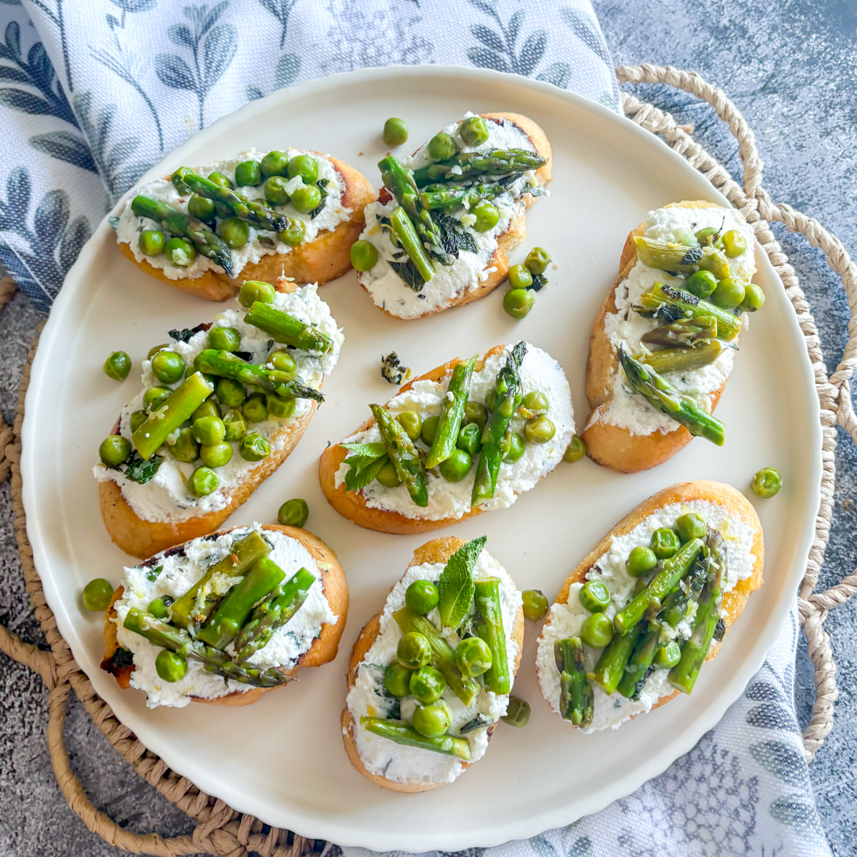 Plated pea and asparagus crostini with whipped lemon ricotta and fresh spring vegetables on a white dish