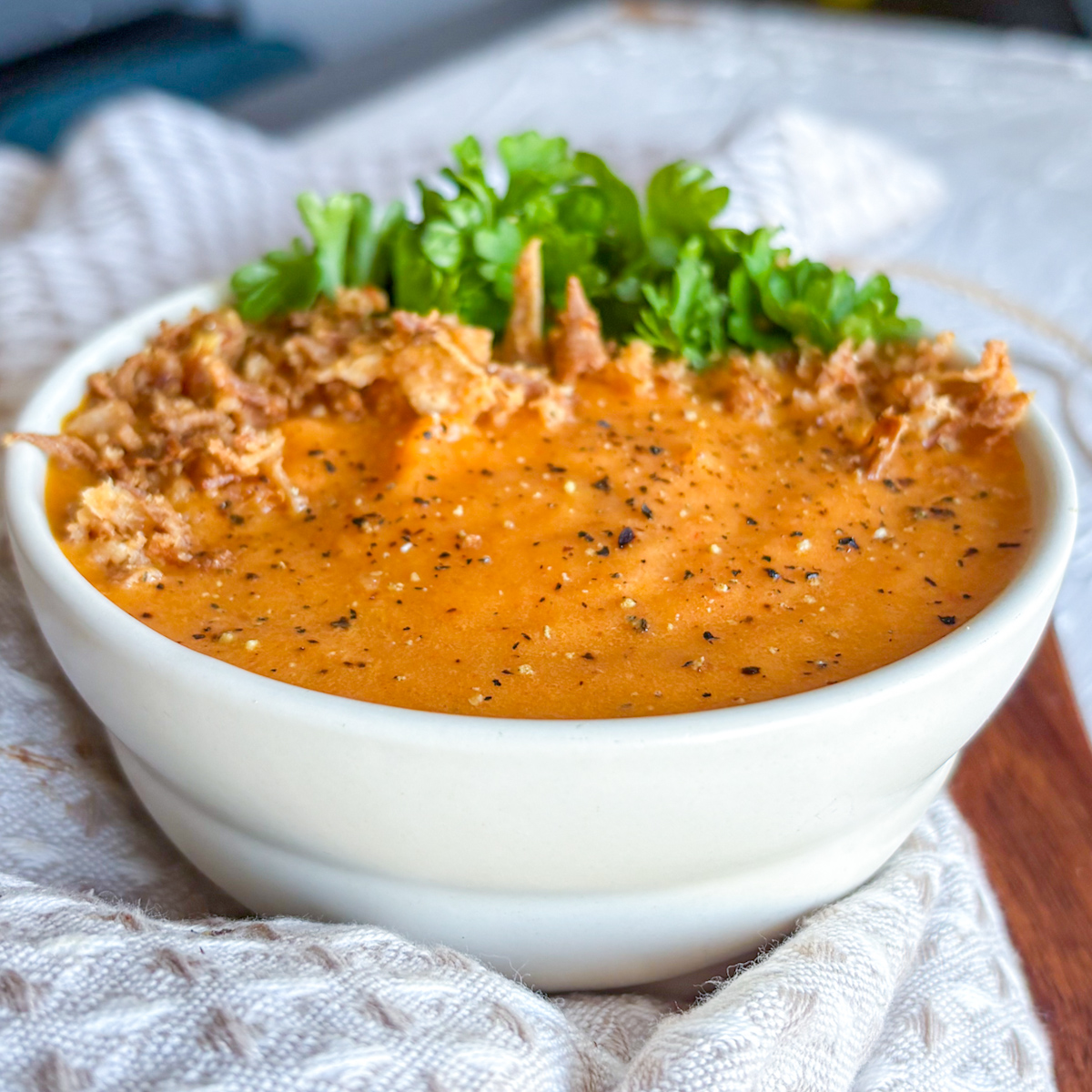 Easy roasted carrot and ginger soup recipe in a white bowl with parsley and crispy onion topping.