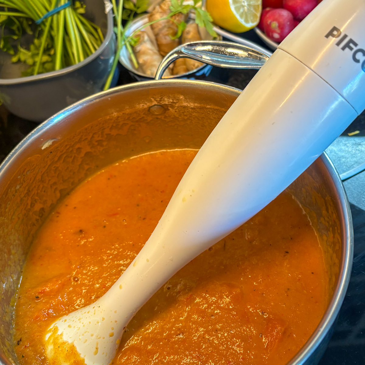  Blending the roasted carrot and ginger soup with a stick blender in a stainless steel pot.