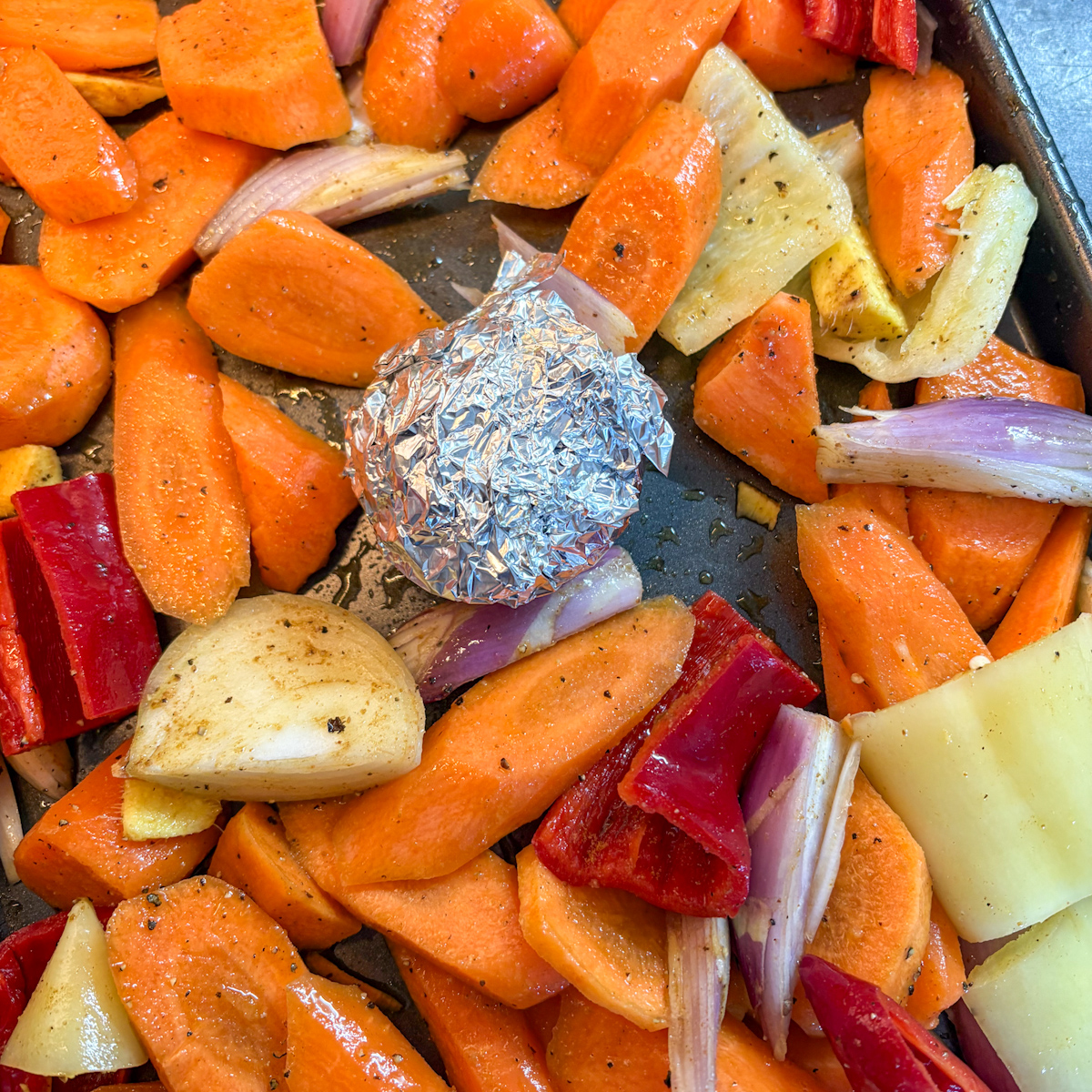  Raw chopped carrots, peppers, shallots and foil-wrapped garlic on a roasting tray for carrot soup.