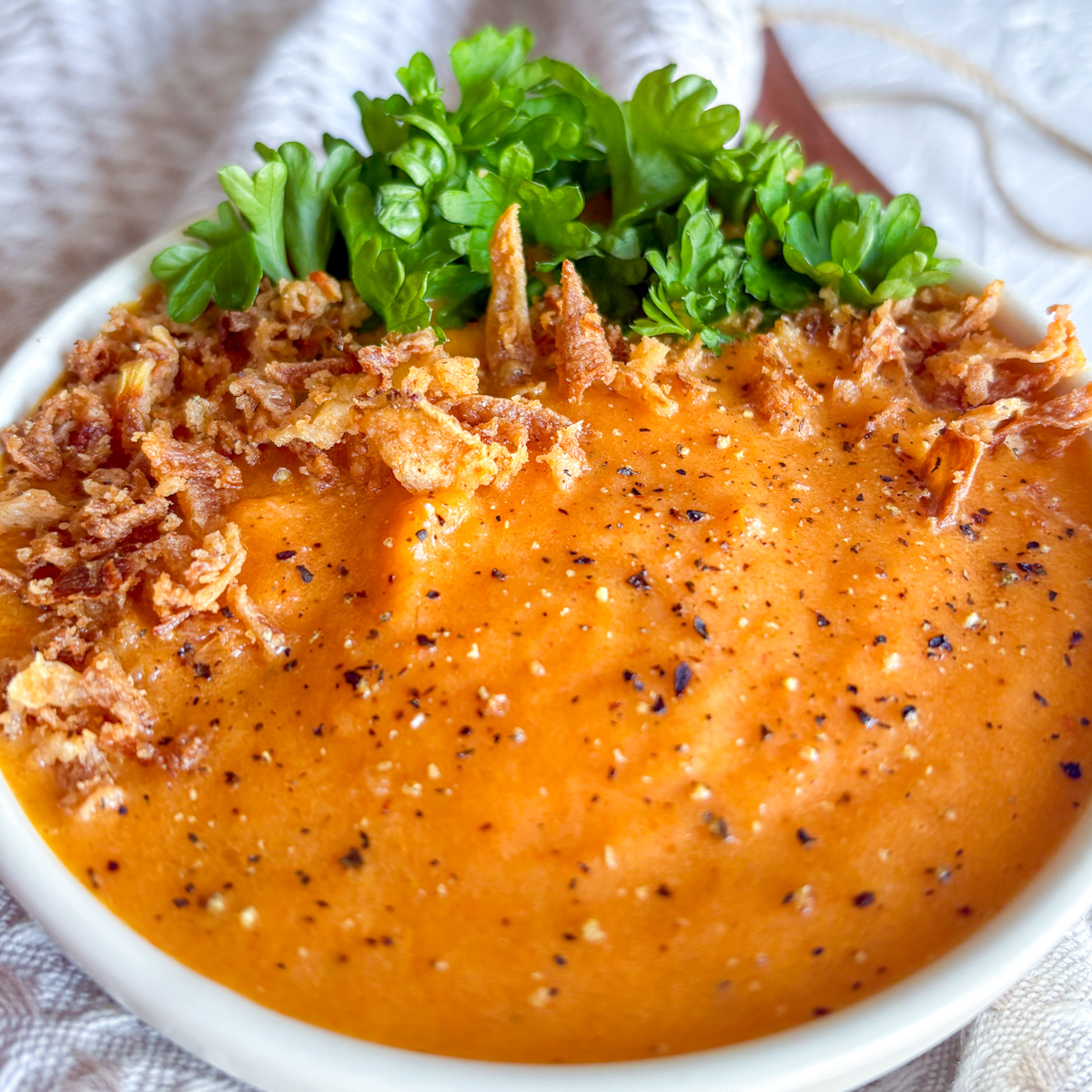 Close-up of creamy roasted carrot and ginger soup with crispy onions and ground black pepper.