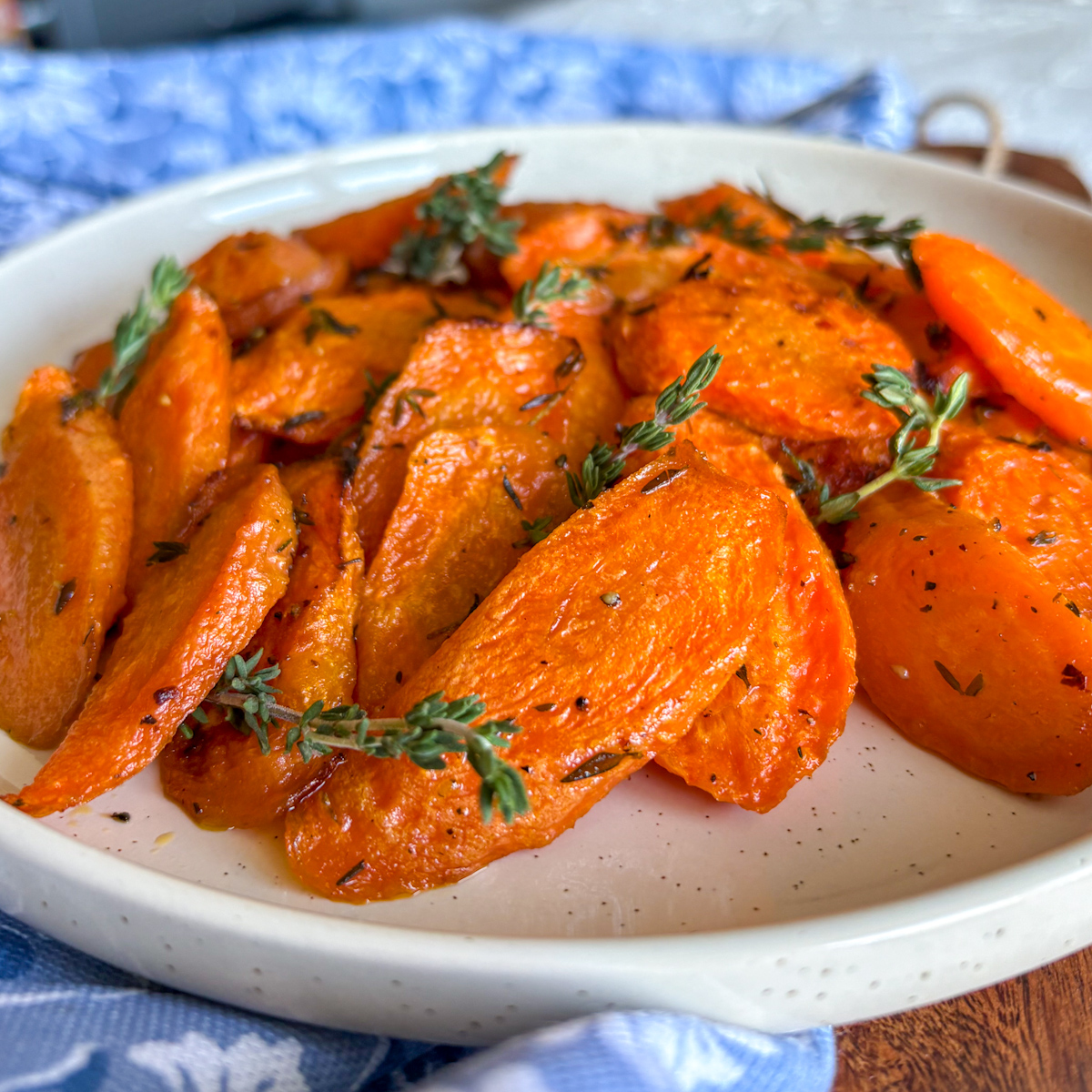 Herb roasted carrots with thyme in speckled white bowl, top-down view on wooden board
