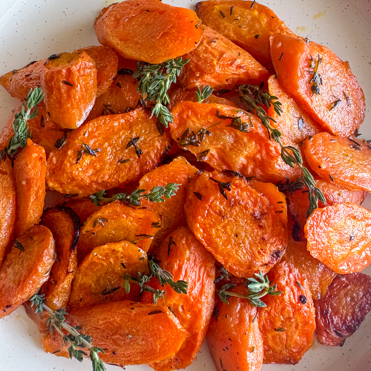 Close-up of roasted carrots with thyme garnished with fresh thyme sprigs in a white bowl