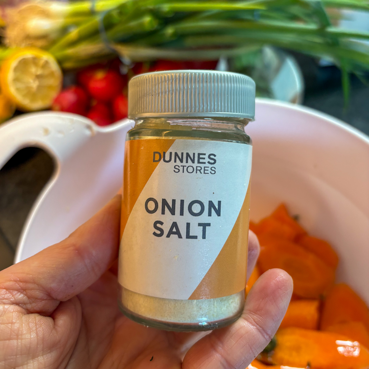 Onion salt jar held over bowl of sliced carrots, ingredient prep for roasted carrots recipe