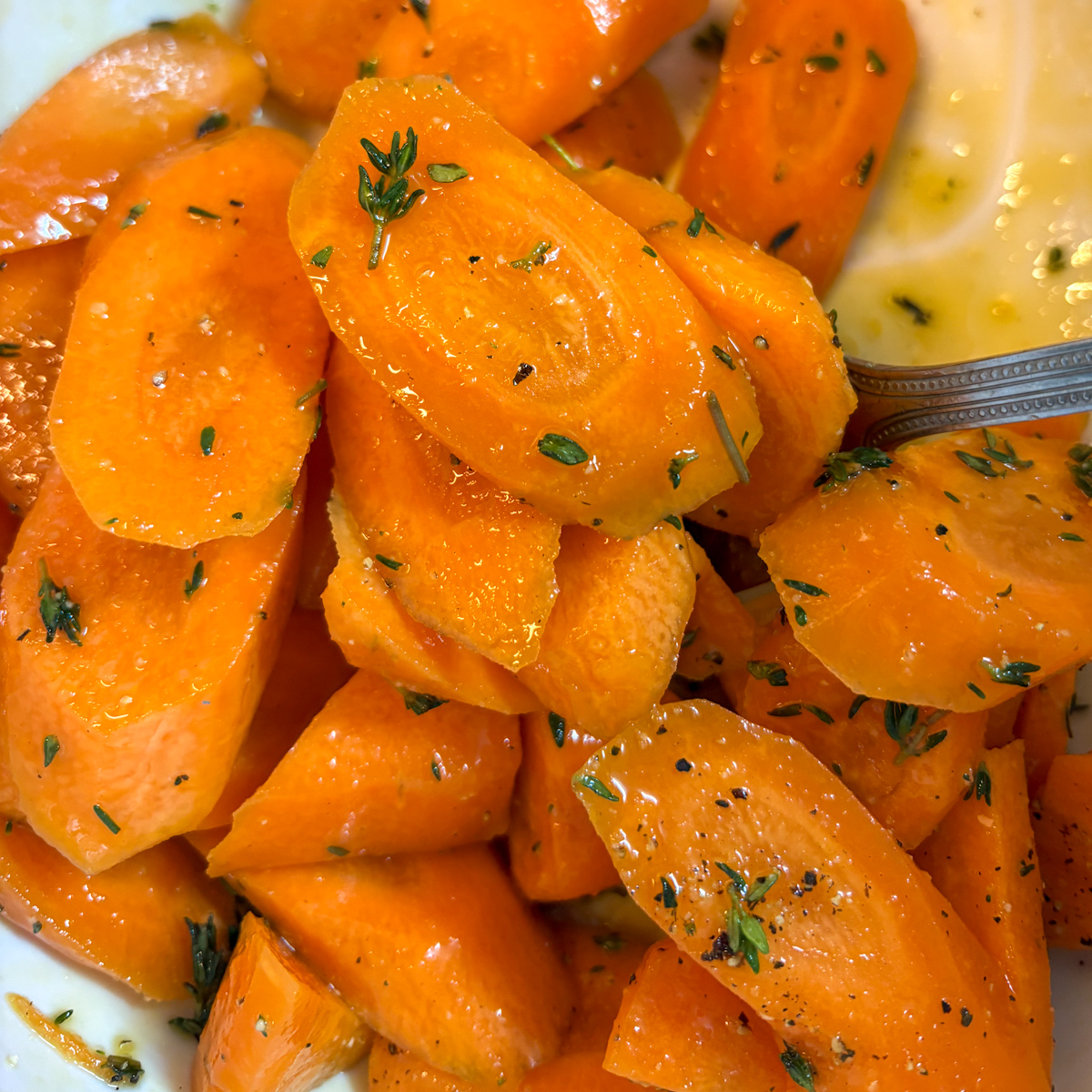 Sliced carrots tossed with olive oil, thyme and onion salt in pink bowl ready for roasting