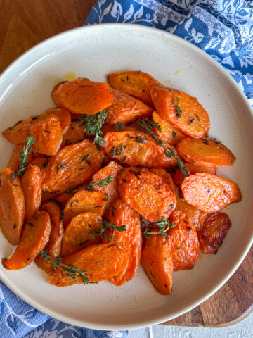 Thyme roasted carrots on white oval plate with blue floral napkin and fresh thyme garnish