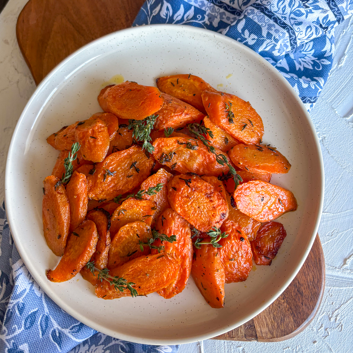 Thyme roasted carrots on white oval plate with blue floral napkin and fresh thyme garnish