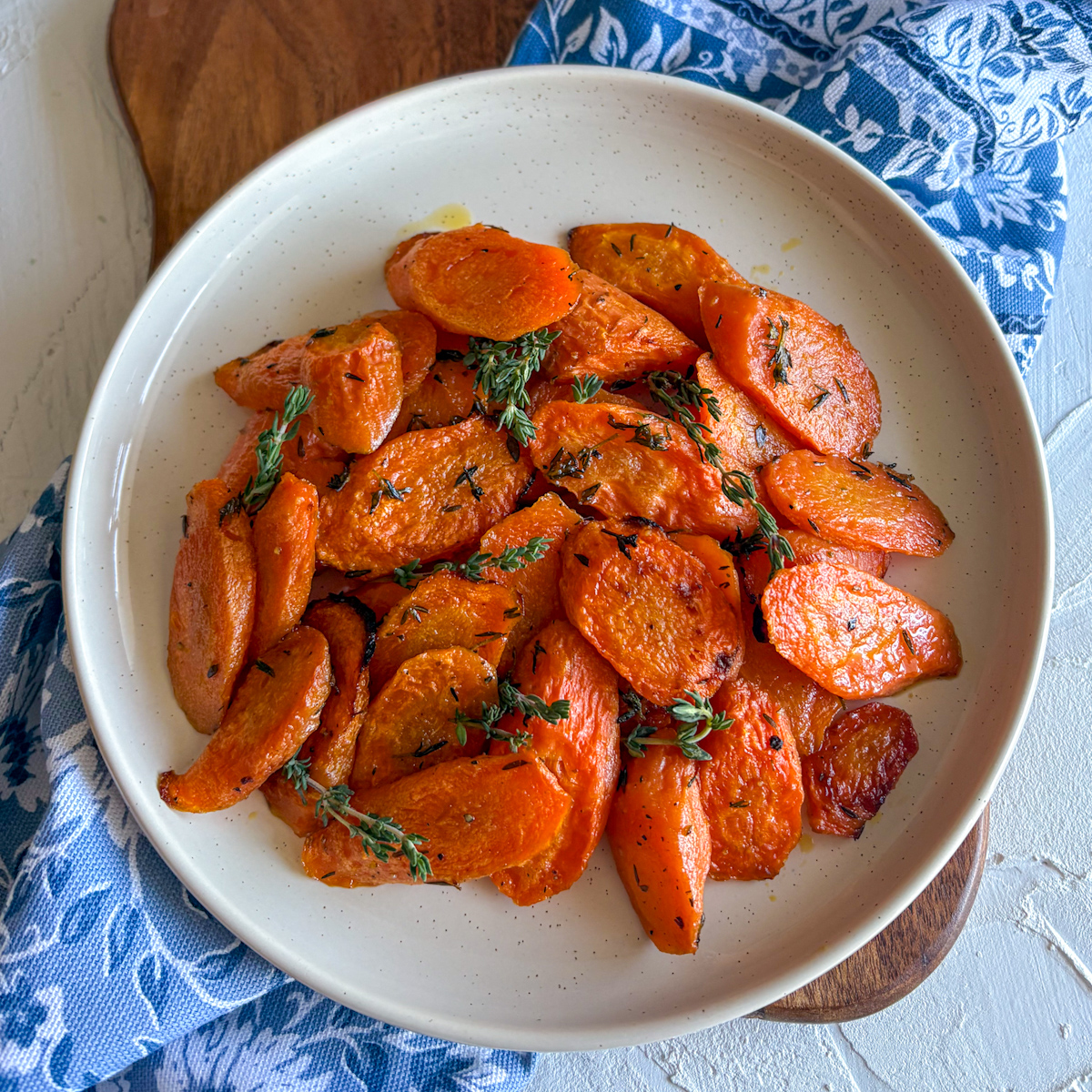  Herb roasted carrots with thyme in speckled white bowl, top-down view on wooden board