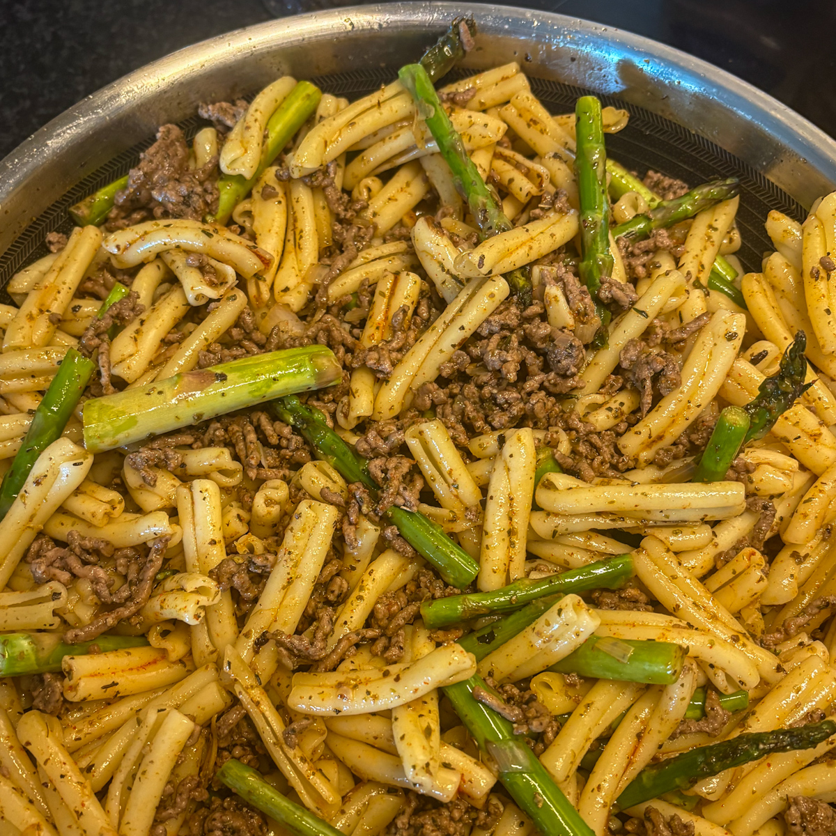Beef and asparagus pasta cooking in a large skillet with lean mince, herbs and asparagus pieces