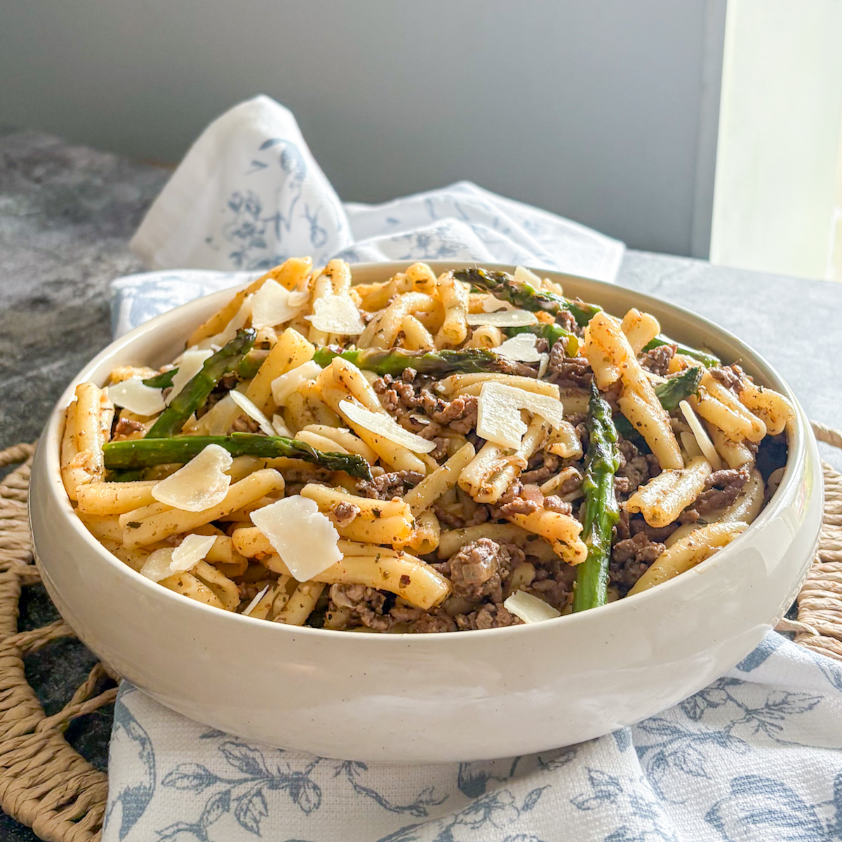 Beef and asparagus pasta recipe served in a ceramic bowl with parmesan shavings and aromatic herbs