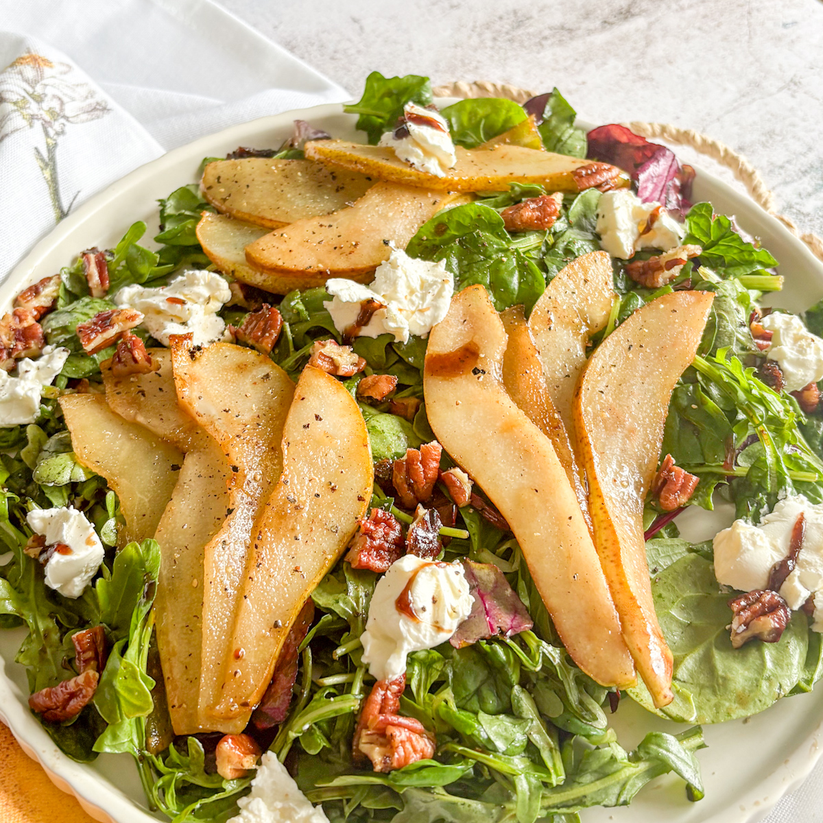 Caramelised pear salad on a white plate with pecans, mascarpone and a balsamic drizzle