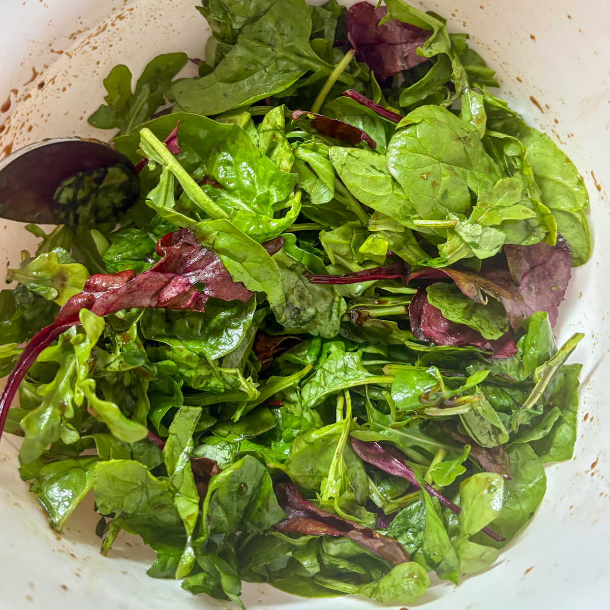 Dressed mixed salad leaves in a bowl with balsamic glaze for caramelised pear salad