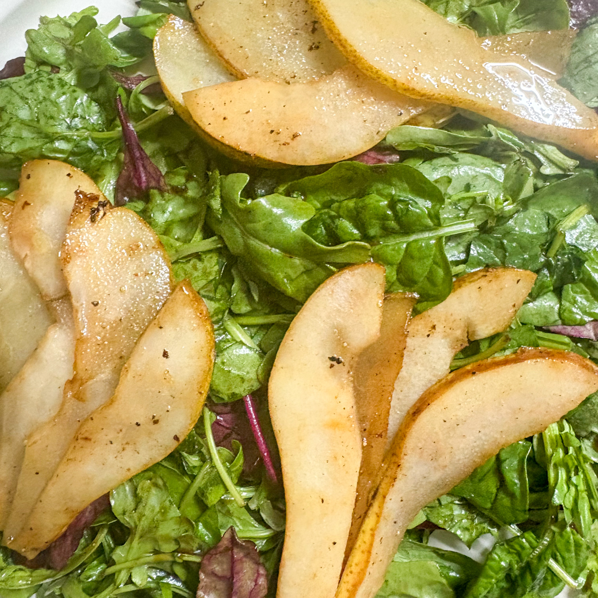 Close-up pan-fried caramelised pear slices on mixed baby leaves for caramelised pear salad