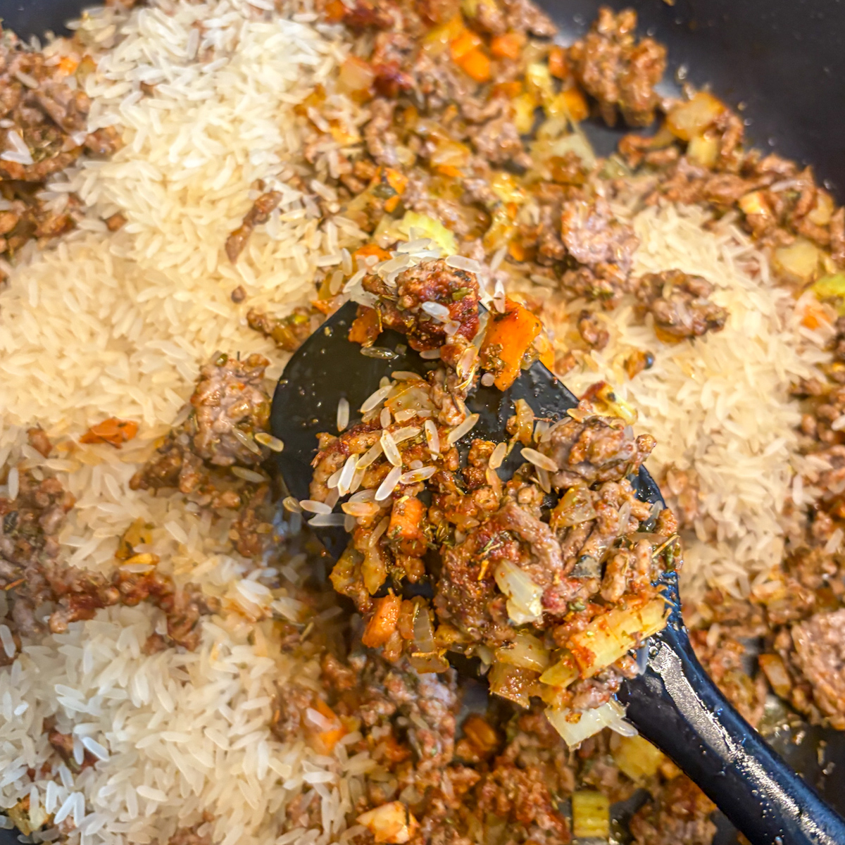 Spatula lifting browned mince and vegetables over rice for dirty rice with beef mince