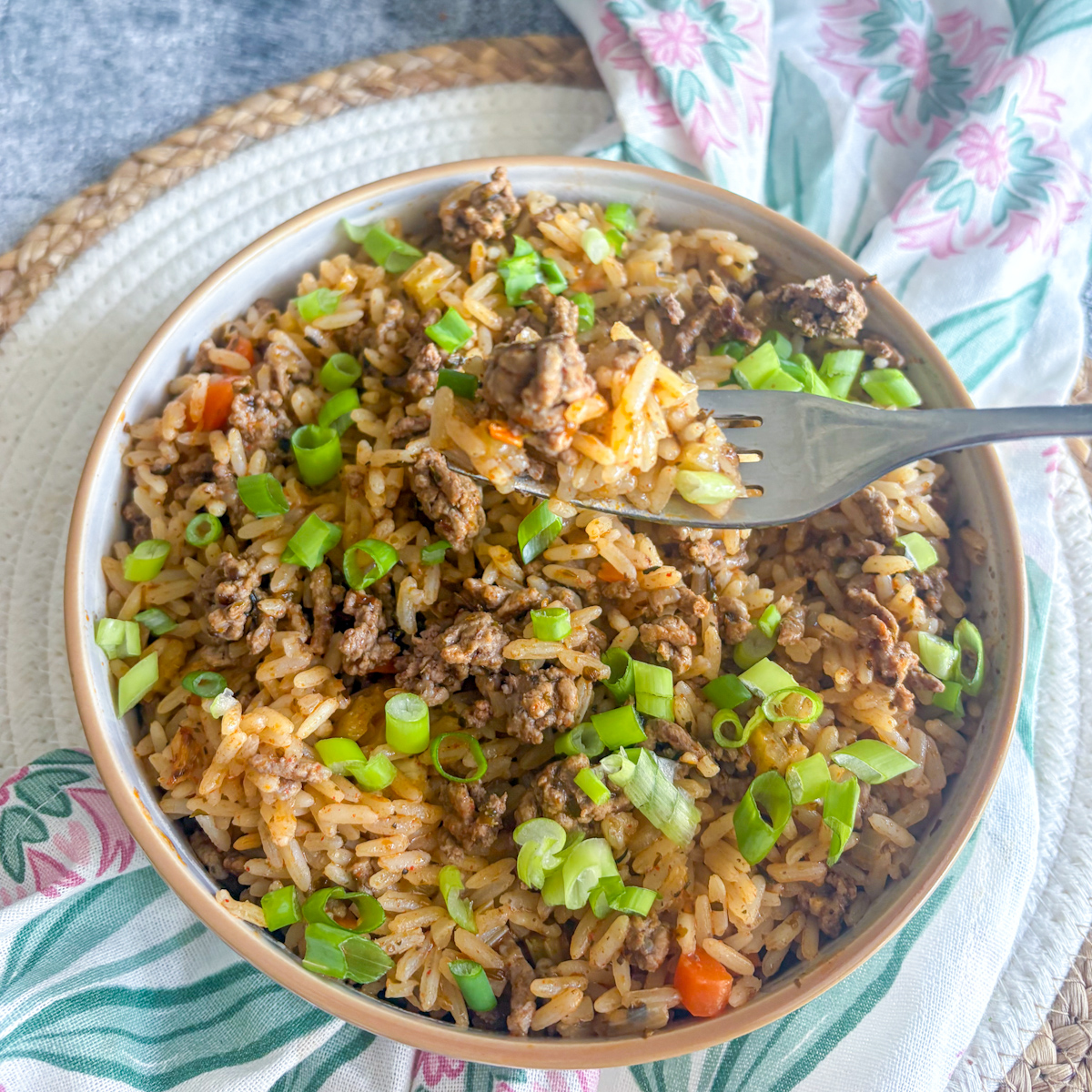 Dirty rice with beef mince in a bowl with a fork lifting a portion, topped with spring onions
