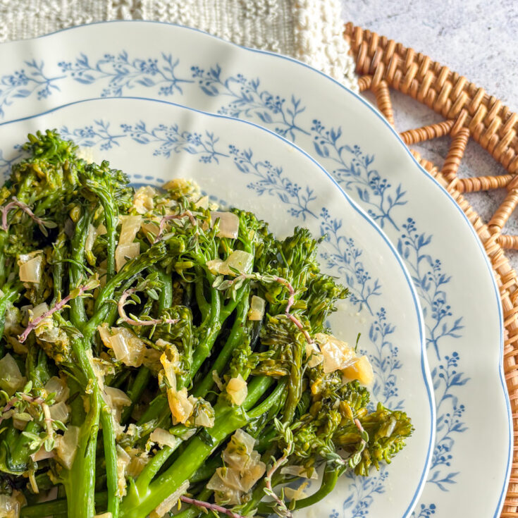 Close-up of glossy pan-steamed broccolini with shallots and thyme leaves