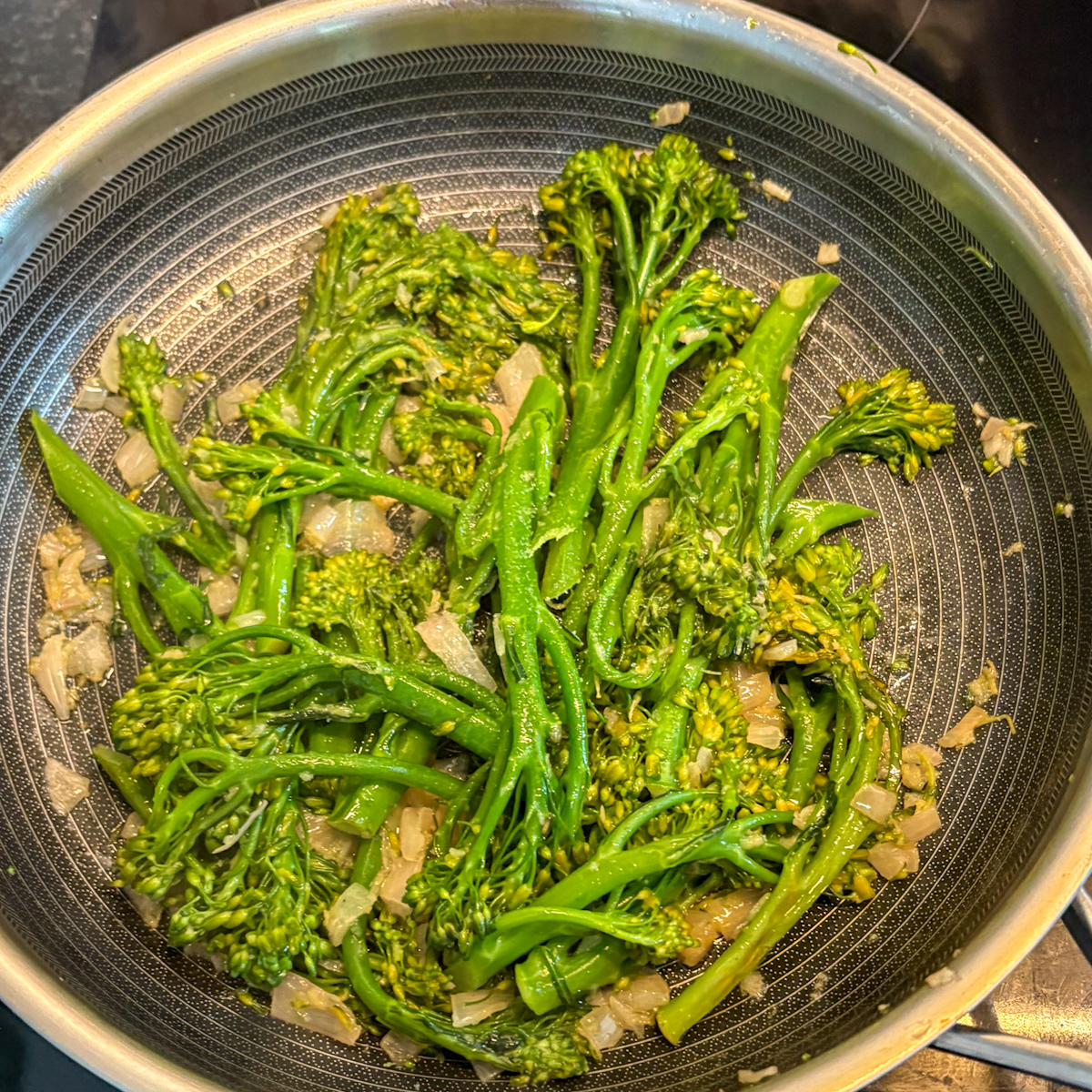 Pan-steamed broccolini cooking with shallots and garlic in a deep skillet
