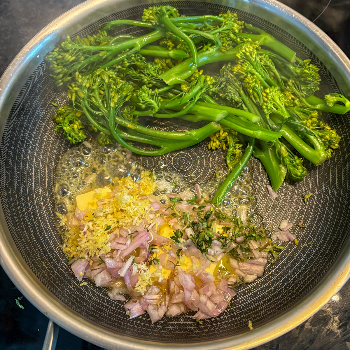 Adding butter, shallot, lemon zest and thyme to pan-steamed broccolini in skillet