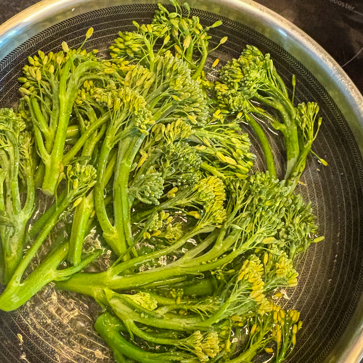 Broccolini stalks steaming in a deep skillet for the pan-steamed broccolini recipe