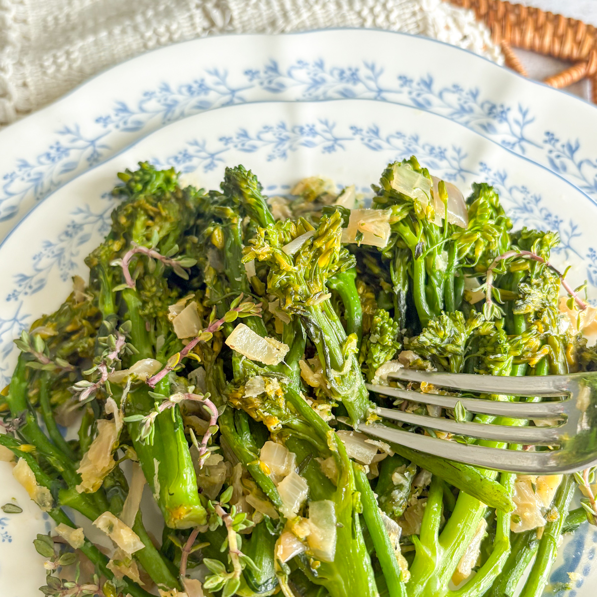 Pan-steamed broccolini with shallot and thyme on a blue patterned plate with fork
